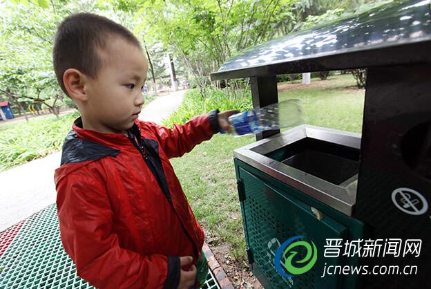 一位小朋友正在将废弃的饮用水瓶丢到垃圾筒内。